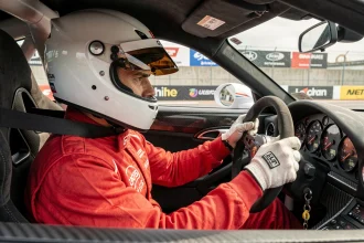 Pilote amateur en combinaison de course rouge au volant d'une Porsche 911 GT3 Cup dans les stands d'un circuit automobile