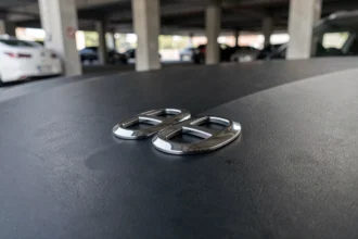 Gros plan sur un sigle chromé de voiture de luxe monté sur un capot noir mat, reflets métalliques et texture précise